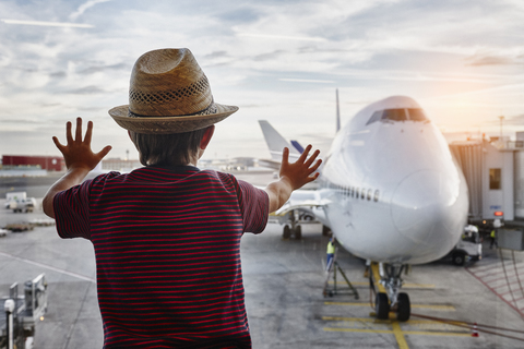 Boy wearing straw hat looking through window to airplane on the apron stock photo