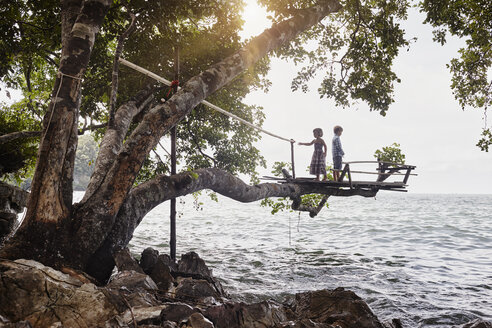 Thailand, Railay, Rai Leh East Beach, Junge und kleines Mädchen auf Baumhaus über dem Meer - RORF01073