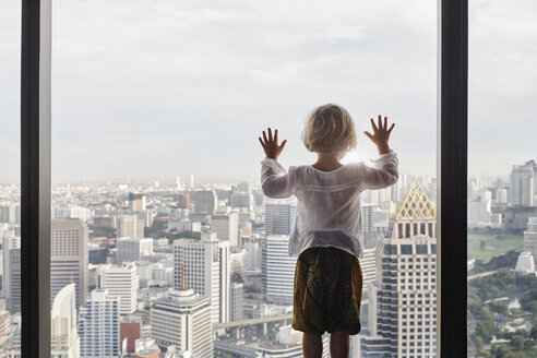 Thailand, Bangkok, kleines Mädchen schaut durch ein Fenster auf eine Stadtlandschaft - RORF01080