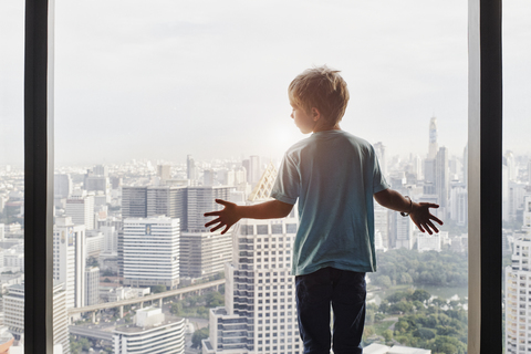 Thailand, Bangkok, Junge schaut durch ein Fenster auf eine Stadtlandschaft, lizenzfreies Stockfoto