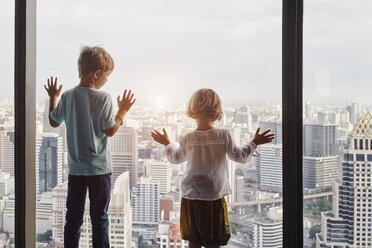Thailand, Bangkok, Junge und kleines Mädchen schauen durch ein Fenster auf eine Stadtlandschaft - RORF01083