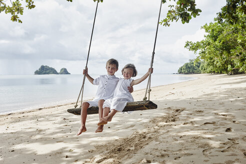 Thailand, Ko Yao Noi, glücklicher Junge und kleines Mädchen auf einer Schaukel am Strand - RORF01087