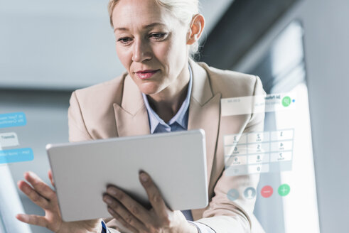 Businesswoman sitting in office, using digital tablet - UUF12531