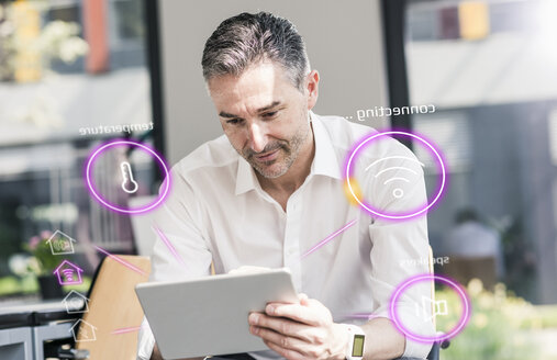 Man sitting in office, using digital tablet to remote-control his smart home - UUF12536