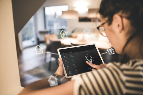 Woman sitting at home, using digital tablet to remote-control his smart home - UUF12538