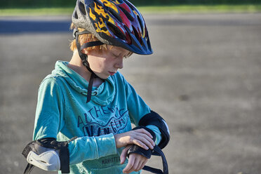 Boy wearing helmet putting on elbow pads - JEDF00298