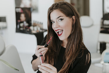 Portrait of young woman applying lipstick - OCAF00051