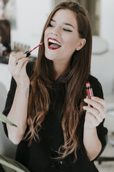 Porträt einer glücklichen jungen Frau, die Lippenstift aufträgt - OCAF00052