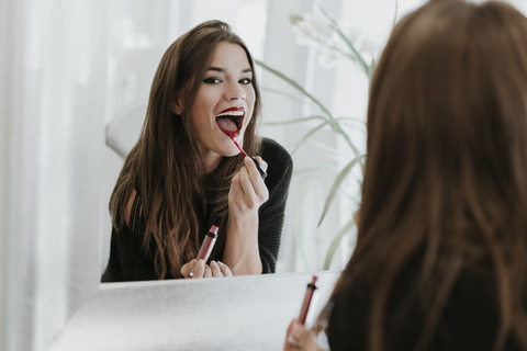 Spiegelbild einer jungen Frau, die Lippenstift aufträgt, lizenzfreies Stockfoto