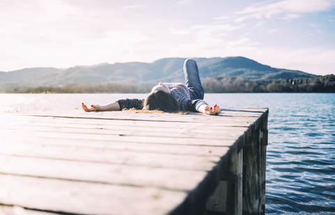 Frau ruht sich auf einem Holzsteg an einem See aus, lizenzfreies Stockfoto