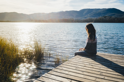 Woman sitting on a wooden platform at a lake at sunset stock photo