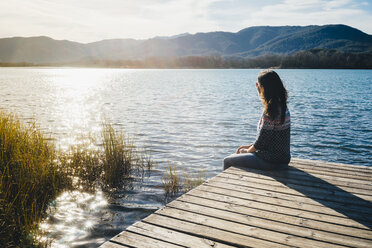 Woman sitting on a wooden platform at a lake at sunset - GEMF01855