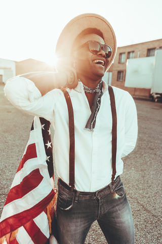 Porträt eines lachenden jungen Mannes mit amerikanischer Flagge im Gegenlicht, lizenzfreies Stockfoto