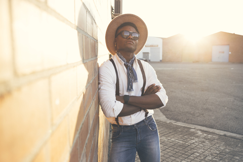 Portrait of cool young man wearing hat and sunglasses leaning against wall stock photo