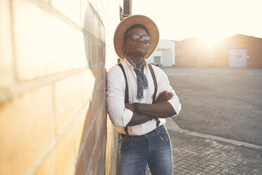 Porträt eines coolen jungen Mannes mit Hut und Sonnenbrille, der an der Wand lehnt - OCAF00070