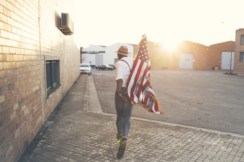 Rückenansicht eines jungen Mannes, der mit einer amerikanischen Flagge im Gegenlicht läuft, lizenzfreies Stockfoto