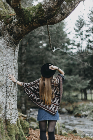 Back view of young woman wearing hat and poncho in autumnal forest stock photo