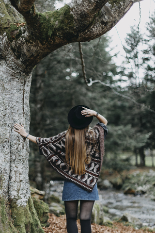Rückenansicht einer jungen Frau mit Hut und Poncho in einem herbstlichen Wald, lizenzfreies Stockfoto