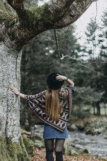 Back view of young woman wearing hat and poncho in autumnal forest - OCAF00074