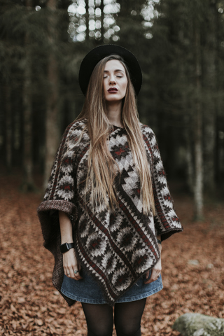 Portrait of young woman wearing hat and poncho standing in autumnal forest stock photo