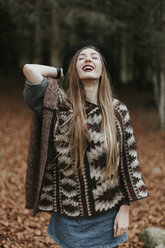 Portrait of laughing of young woman wearing hat and poncho in autumnal forest - OCAF00077