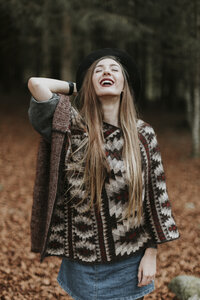 Porträt einer lachenden jungen Frau mit Hut und Poncho in einem herbstlichen Wald - OCAF00077