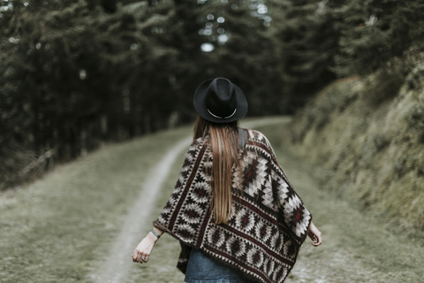 Back view of fashionable young woman wearing hat and poncho in nature stock photo