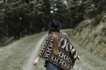 Back view of fashionable young woman wearing hat and poncho in nature - OCAF00089