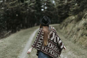 Rückenansicht einer modischen jungen Frau mit Hut und Poncho in der Natur - OCAF00089