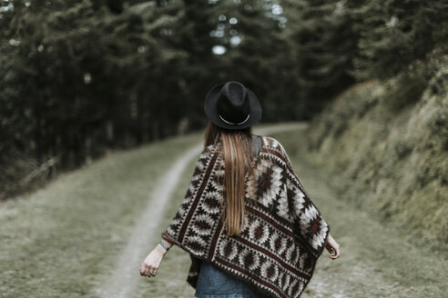 Rückenansicht einer modischen jungen Frau mit Hut und Poncho in der Natur - OCAF00089