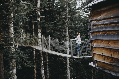 Junge Frau auf einer Hängebrücke am Baumhaus im Wald, lizenzfreies Stockfoto