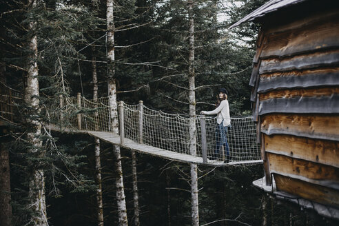 Junge Frau auf einer Hängebrücke am Baumhaus im Wald - OCAF00095