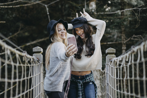 Two happy young women on a suspension bridge taking a selfie stock photo