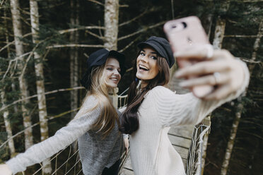 Zwei glückliche junge Frauen auf einer Hängebrücke machen ein Selfie - OCAF00100