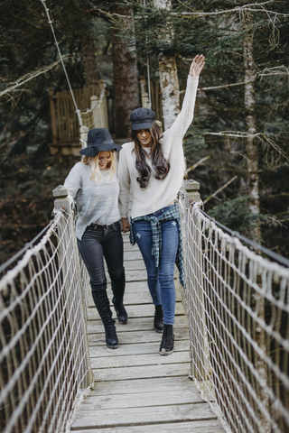Two happy young women walking on a suspension together stock photo