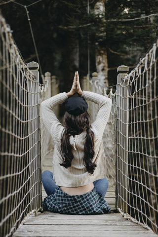 Junge Frau in Yoga-Pose auf einer Hängebrücke sitzend, lizenzfreies Stockfoto