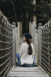 Lächelnde junge Frau auf einer Hängebrücke sitzend - OCAF00104
