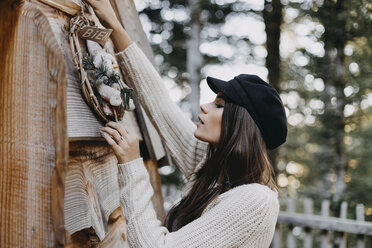 Young woman decorating wooden house with Christmas decoration - OCAF00106