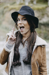 Portrait of happy young woman wearing flappy hat and smoking a cigarette in the nature - OCAF00115