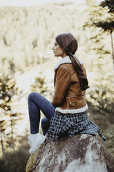 Junge Frau sitzt auf einem Baumstamm in der Natur - OCAF00119