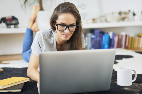 Young woman at home lying on the floor using laptop stock photo