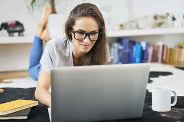 Junge Frau zu Hause auf dem Boden liegend mit Laptop - BSZF00144