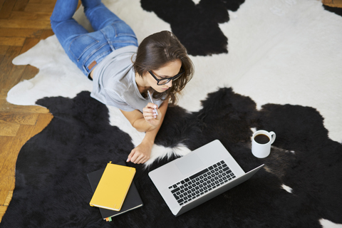 Junge Frau zu Hause auf dem Boden liegend mit Laptop, lizenzfreies Stockfoto