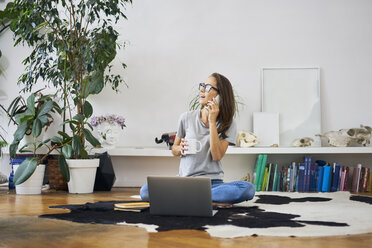 Young woman at home sitting on the floor talking on cell phone - BSZF00149