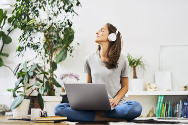 Relaxed young woman at home sitting on the floor using laptop and listening to music - BSZF00151