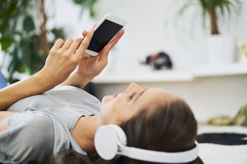 Junge Frau auf dem Boden liegend mit Kopfhörern und Mobiltelefon, lizenzfreies Stockfoto