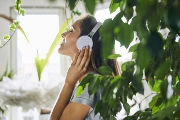 Smiling young woman with headphones listening to music at indoor plant - BSZF00157