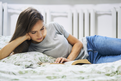 Young woman at home lying in bed reading book stock photo