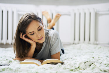 Young woman at home lying in bed reading book - BSZF00160