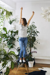 Young woman standing on chair in a room cheering - BSZF00161